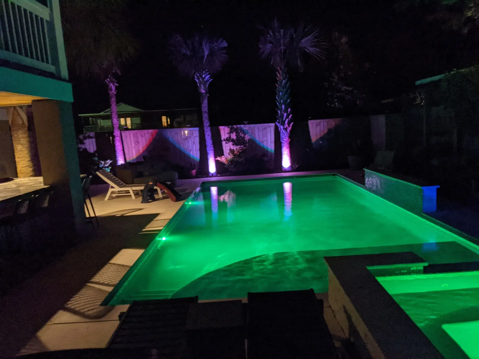 Pool glowing green with palms uplit in pink at night