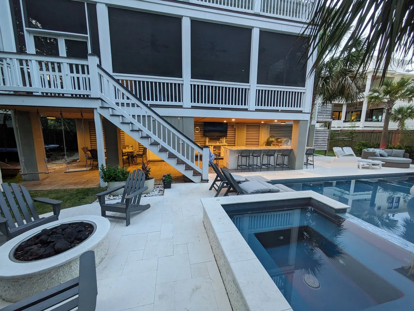 Fire pit, hot tub and the lit outdoor bar under the porches at dusk