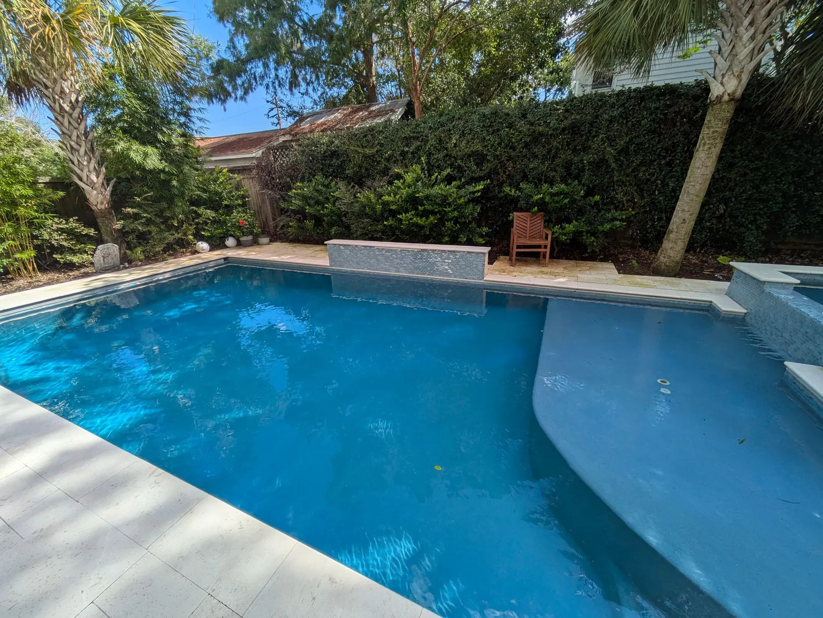 Bright blue pool with a sun shelf and a waterfall wall